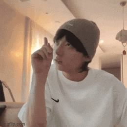 a man wearing a beanie and a white shirt is giving a thumbs up sign .