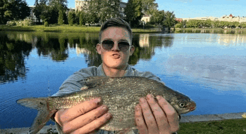 a man wearing sunglasses is holding a large fish in his hands