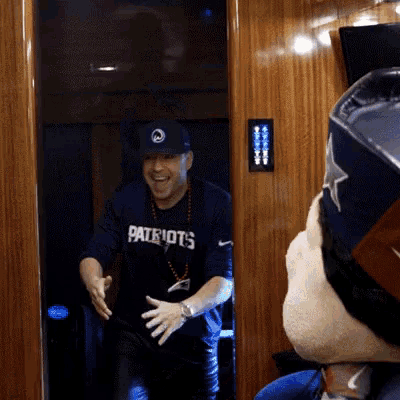 a man wearing a patriots shirt is standing in a doorway