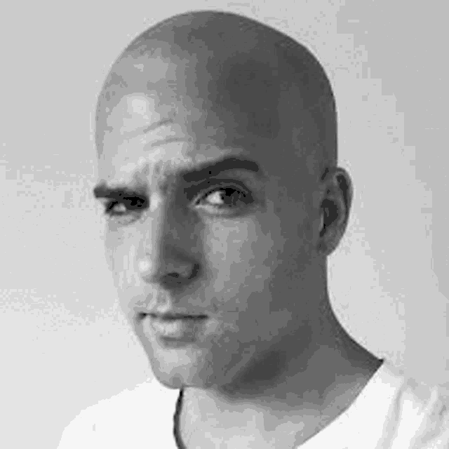 a man with a bald head is wearing a white shirt and looking at the camera .