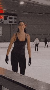 a woman in a black tank top is standing on a rink