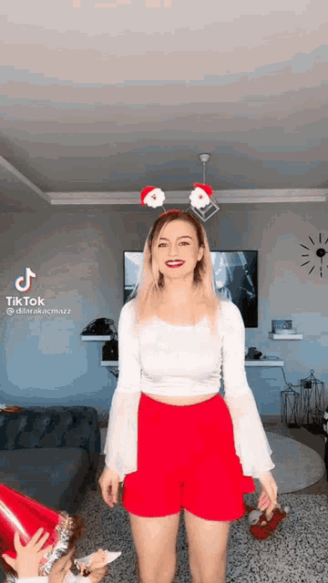 a woman wearing red shorts and a white crop top is standing in a living room .