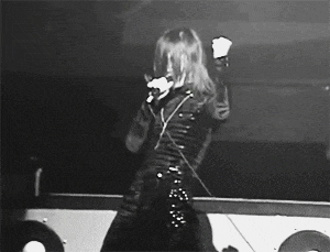 a black and white photo of a woman singing into a microphone on stage .