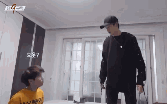 a man in a black hat is standing next to a boy in a yellow shirt in a room .
