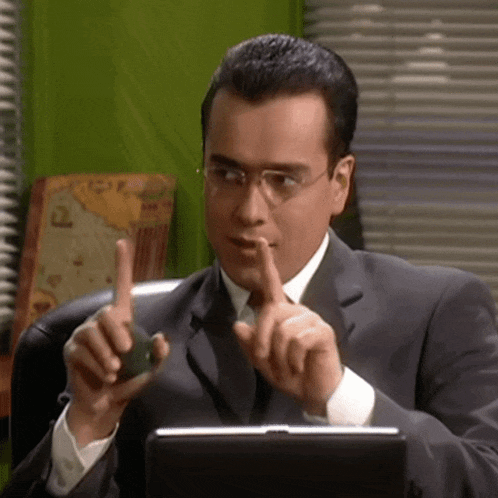 a man in a suit and tie is sitting in front of a laptop and holding his finger to his mouth .