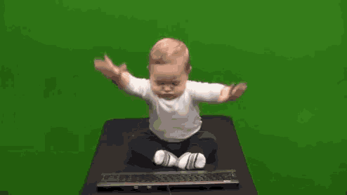 a baby is sitting in front of a computer keyboard on a green screen .