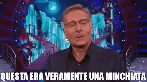 a man in a suit and glasses is standing in front of a waterfall with the words questa era veramente una minchiata below him