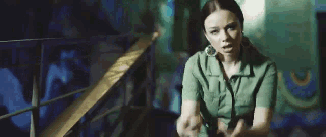 a woman in a green dress is sitting on a staircase holding a microphone and giving the middle finger .