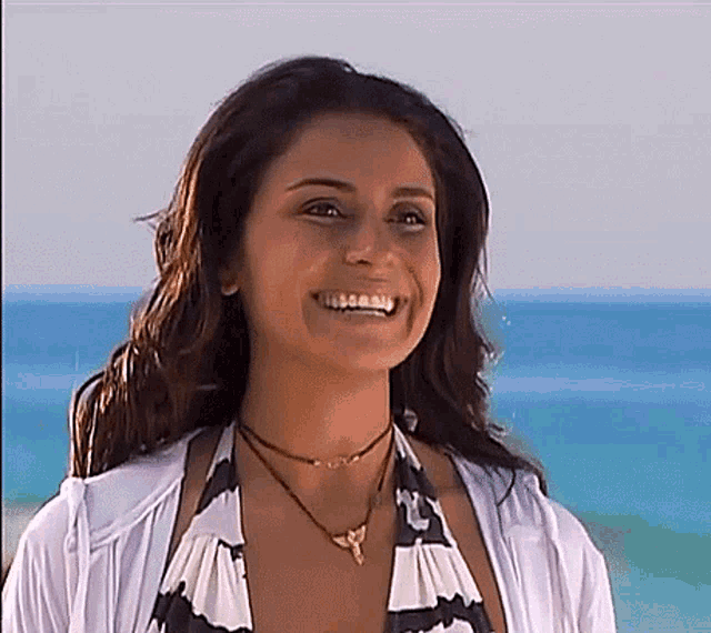 a woman wearing a bikini top and a necklace is smiling on a beach .
