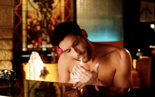 a shirtless man is smoking a cigarette in a dark room