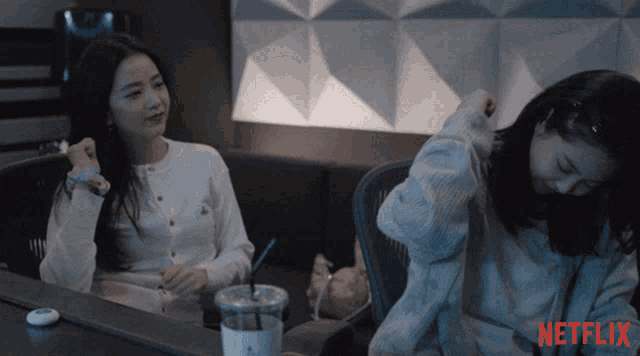 two women sitting at a table with a netflix logo on the bottom right