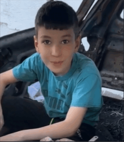 a young boy wearing a blue puma t-shirt is sitting in the driver 's seat of a car .