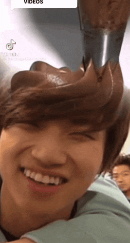 a young man is smiling with a spoon of chocolate on his head behind him