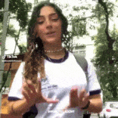 a girl wearing a white shirt with a purple border is standing in front of a building .