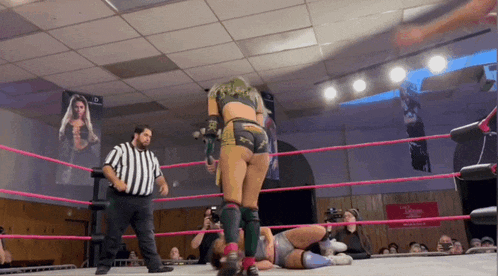 a woman in a wrestling ring with a referee and a sign on the wall that says ' wrestling '