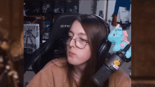 a woman wearing headphones and glasses is sitting in front of a microphone with a stuffed unicorn on her head .