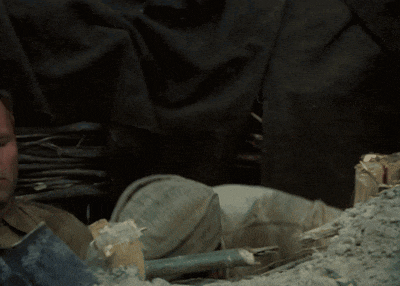 a man is laying in a pile of dirt with a shovel