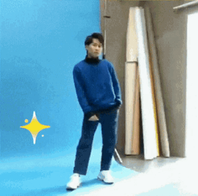 a man in a blue sweater and jeans is standing in front of a blue wall and a yellow star .