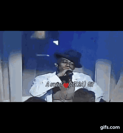 a man is sitting in a chair singing into a microphone with a heart on his chest .