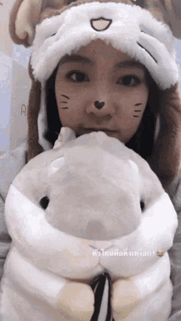 a girl wearing a cat hat holds a stuffed animal in front of her face