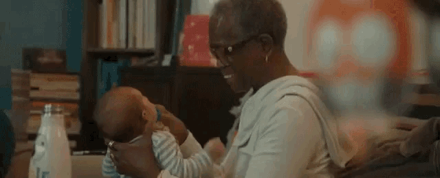 an elderly woman is holding a baby in her lap .
