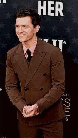 a man in a brown suit and tie is standing on a red carpet .