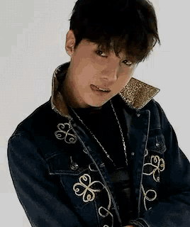 a young man wearing a denim jacket and a necklace is standing in front of a white background .