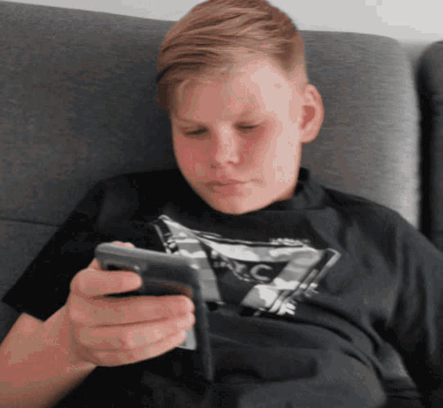a boy wearing a black shirt with the letter c on it looks at his cell phone
