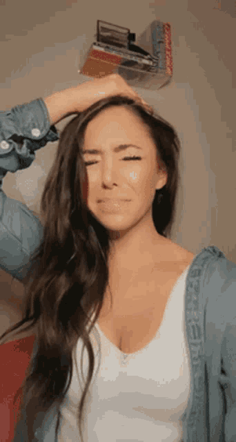 a woman wearing a white tank top and a denim jacket holds her hair