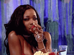 a woman is sitting at a table drinking a glass of wine and eating a strawberry .