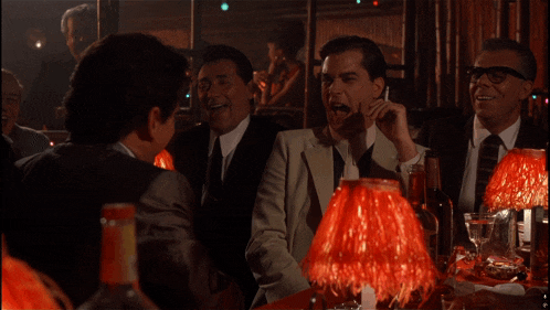 a group of men are sitting at a table with red lamps in a dark room