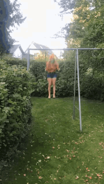 a woman is swinging on a metal swing set in a backyard .