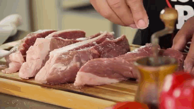 a person is adding salt to a piece of meat on a wooden cutting board .