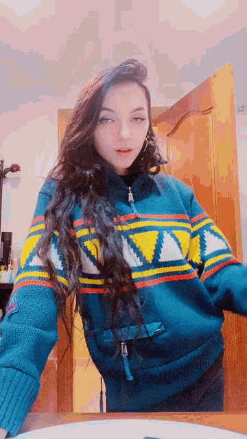 a woman in a blue and yellow sweater is standing in front of a wooden door .