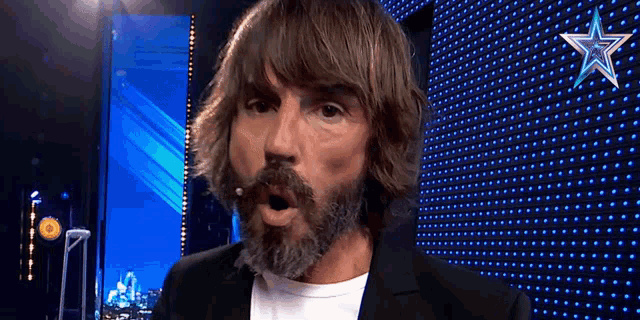 a man with long hair and a beard is standing in front of a blue wall with stars on it