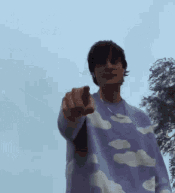 a man wearing a purple sweater with white clouds on it is pointing at the camera .