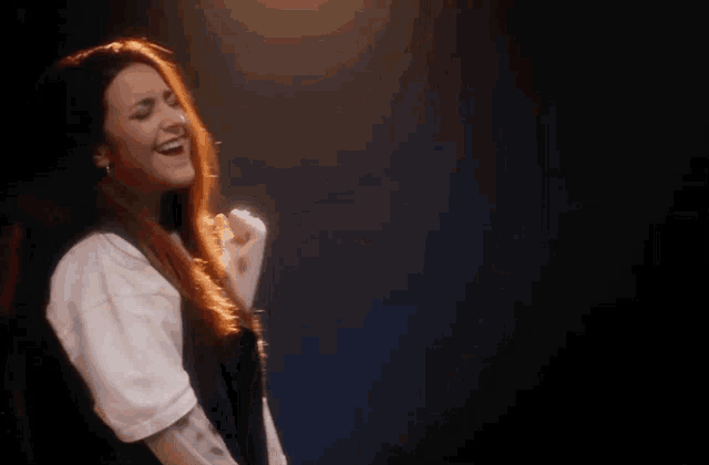 a woman with long red hair is smiling and dancing in a dark room