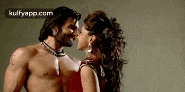 a man and a woman are kissing each other . the man is shirtless and the woman is wearing a red dress .