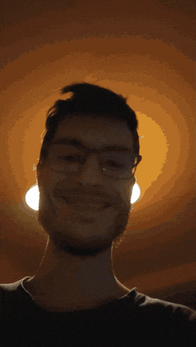 a man with glasses and a beard is smiling in the dark