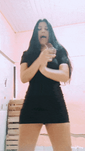 a woman in a black dress is dancing in front of a pink wall with the word imgplay on the bottom right