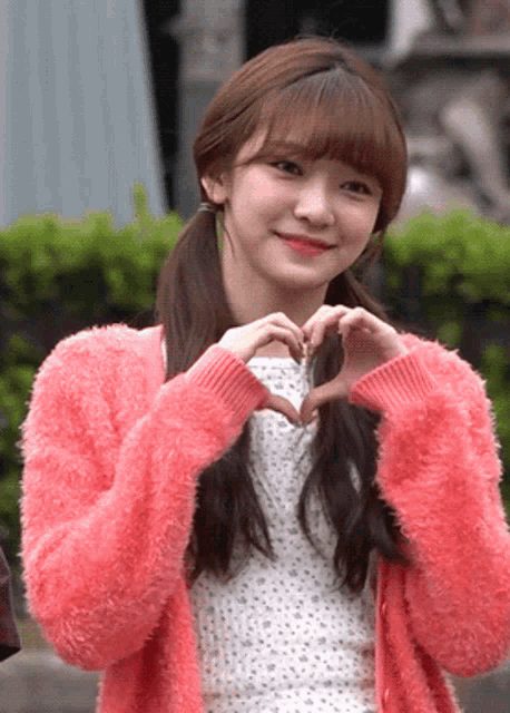 a girl in a pink sweater making a heart with her hands