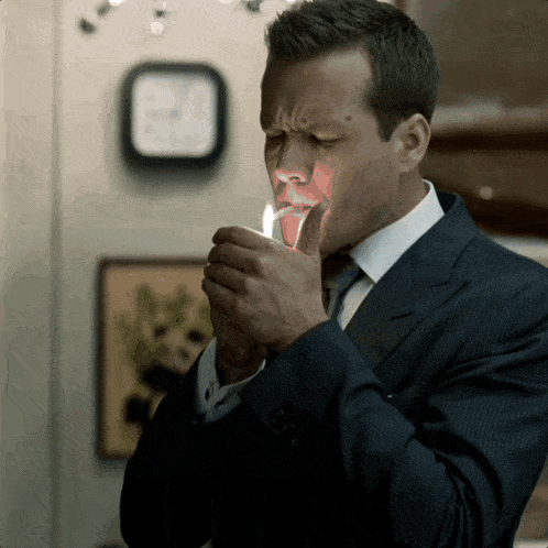 a man in a suit is lighting a cigarette
