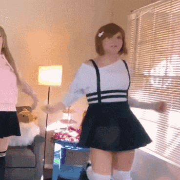 two women are dancing in a living room with blinds on the window