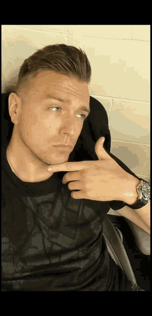 a man wearing a watch and a black shirt is making a funny face