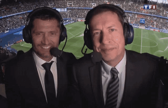 two men wearing headphones in front of a soccer field that says tf1 on the bottom