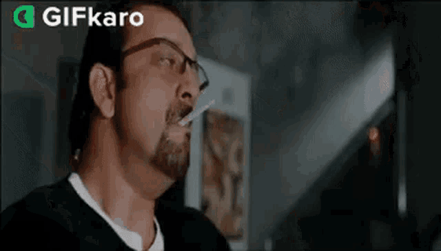 a man with glasses and a beard is smoking a cigarette .
