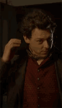 a man wearing a suit and a red vest is standing in a dark room .