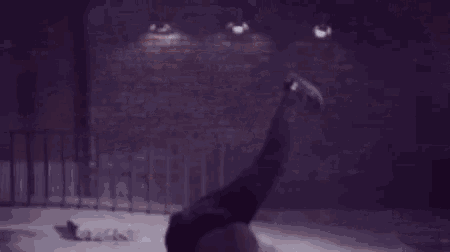 a man wearing a white shirt and a hat is dancing in front of a brick wall .