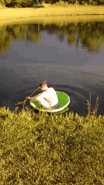 a man is rowing a green raft in a pond