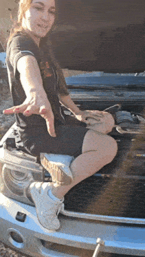 a woman sits on the hood of a car with the hood open